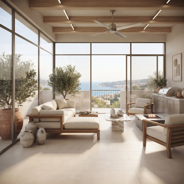 A modern outdoor living room with a large sectional sofa, two armchairs, a low marble coffee table, and a built-in grill area, all in warm neutral tones with a panoramic view of the ocean from floor-to-ceiling windows.
