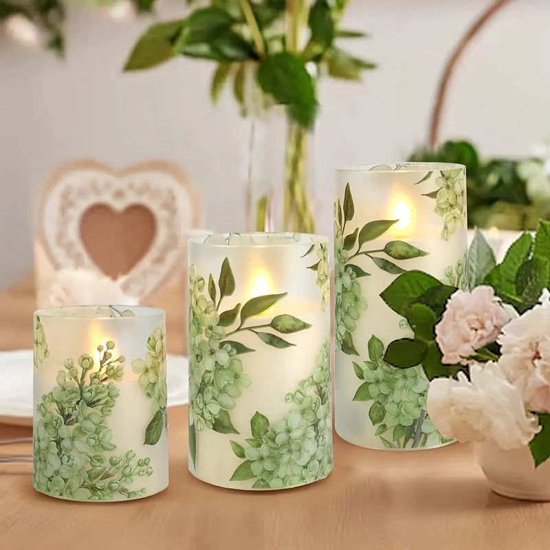 A set of 3 flameless candles, flickering LED pillar candles, with a 10-button remote control. They feature a green floral theme, are suitable for spring and summer, and can be used on the dining tables at wedding venues by House Of Avana