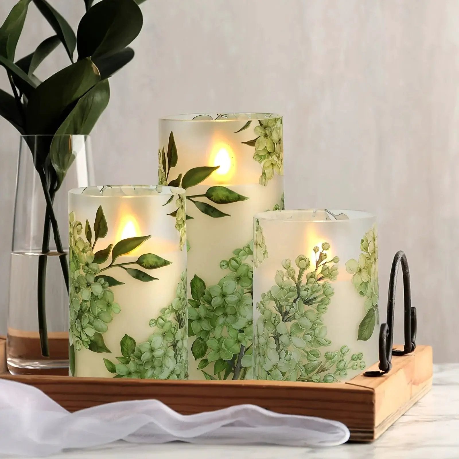 A set of 3 flameless candles, flickering LED pillar candles, with a 10-button remote control. They feature a green floral theme, are suitable for spring and summer, and can be used on the dining tables at wedding venues by House Of Avana